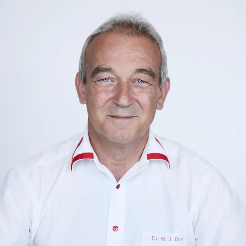 Er lächelt freundlich in die Kamera und trägt ein weisses Hemd mit roten Akzenten.