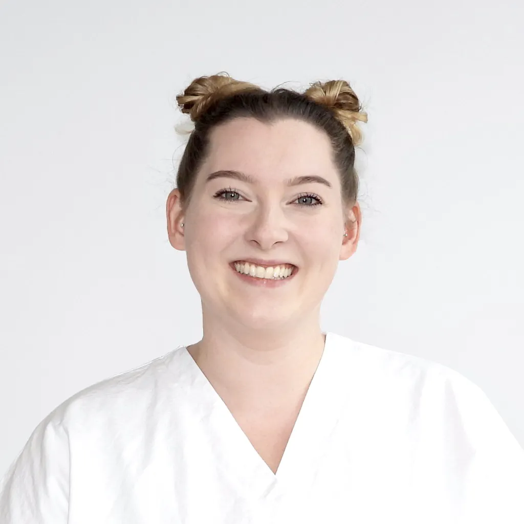 Sie trägt kurzes Haar, ein weisses Oberteil und schaut freundlich in die Kamera.