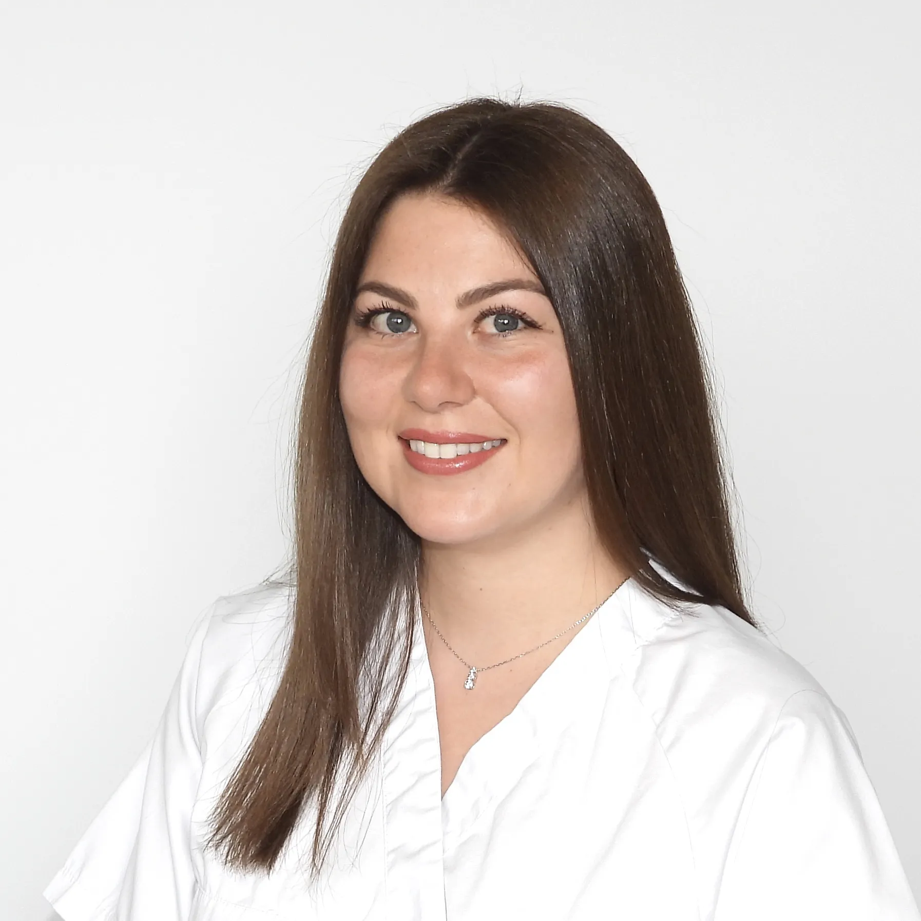 Sie blickt ruhig in die Kamera und trägt ein weisses Oberteil mit offenem Haar.