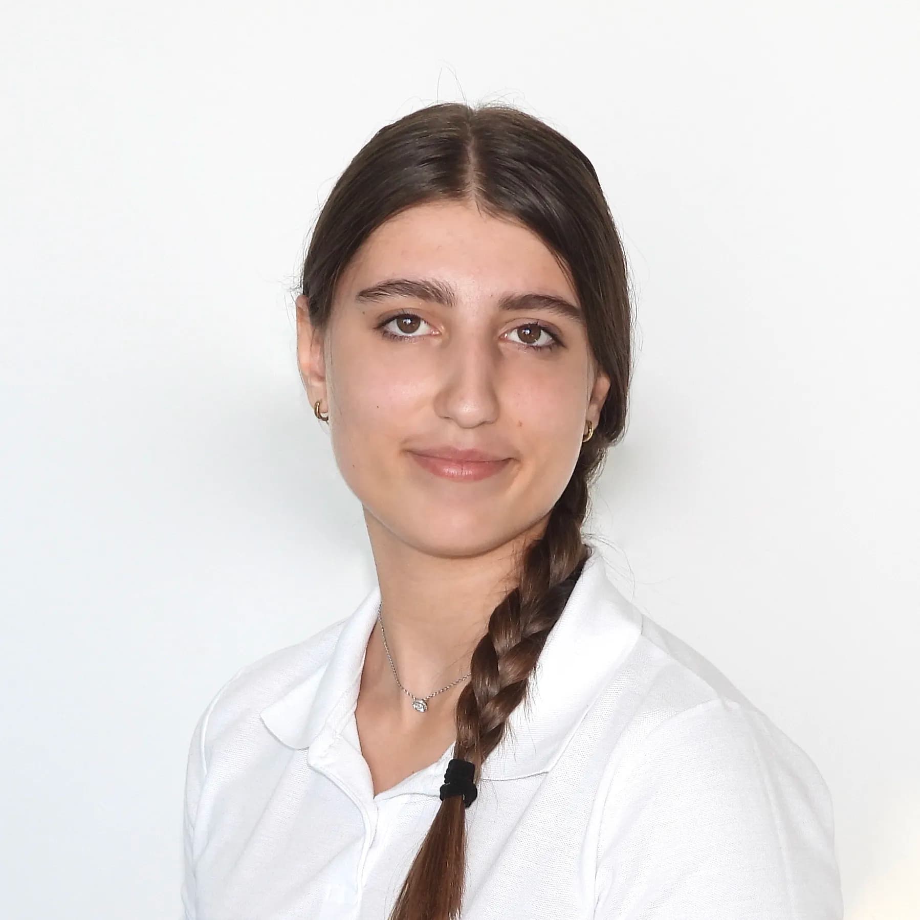 Sie blickt ruhig in die Kamera, trägt ein weisses Oberteil und hat ihr dunkles Haar streng zurückgebunden.