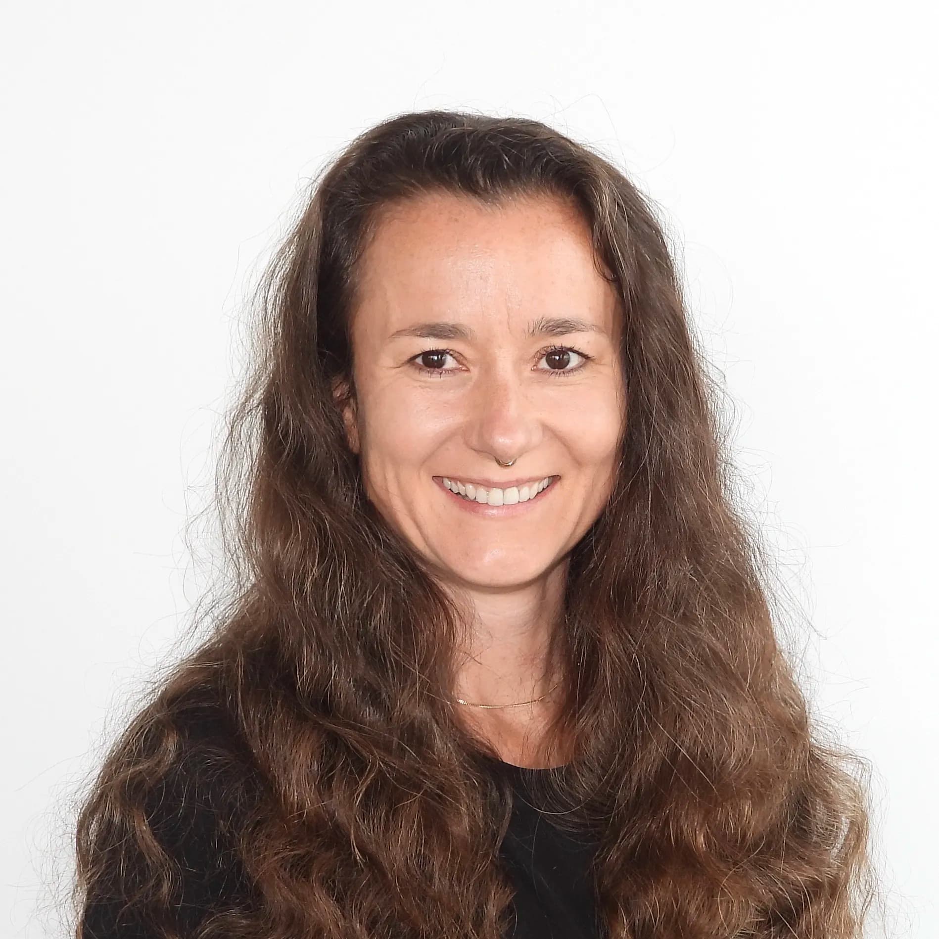 Sie blickt freundlich und hat dunkle, leicht gewellte Haare.